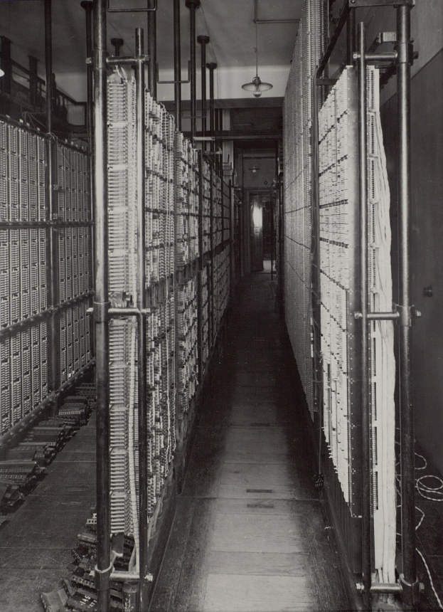 Schwarz-weiß-Foto eines langen Rechenzentrums-Gangs mit Metallrohren, Deckenleuchten und Reihen von Servern.