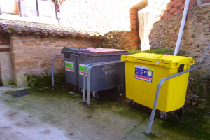 Zwei gelbe und graue Recyclingtonnen mit Rädern stehen nebeneinander vor einem Gebäude mit einer Wand und einem Fenster.