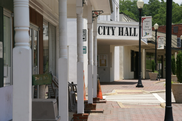 Rathaus mit umliegenden Gebäuden, Straßeninfrastruktur, Fahrzeugen und Vegetation unter einem bewölktem Himmel.