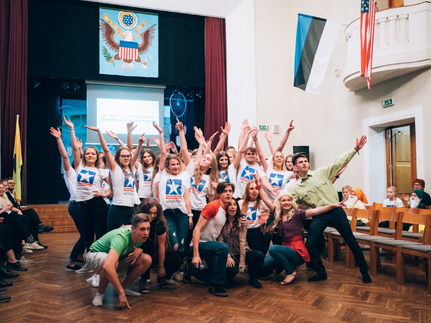 Gruppe von Menschen, die auf einem Foto posieren, bei einem nationalen Jugendkongress-Event, mit einem sitzenden Publikum, Anzeigebildschirm, Flaggen und anderen Event-Details im Hintergrund.