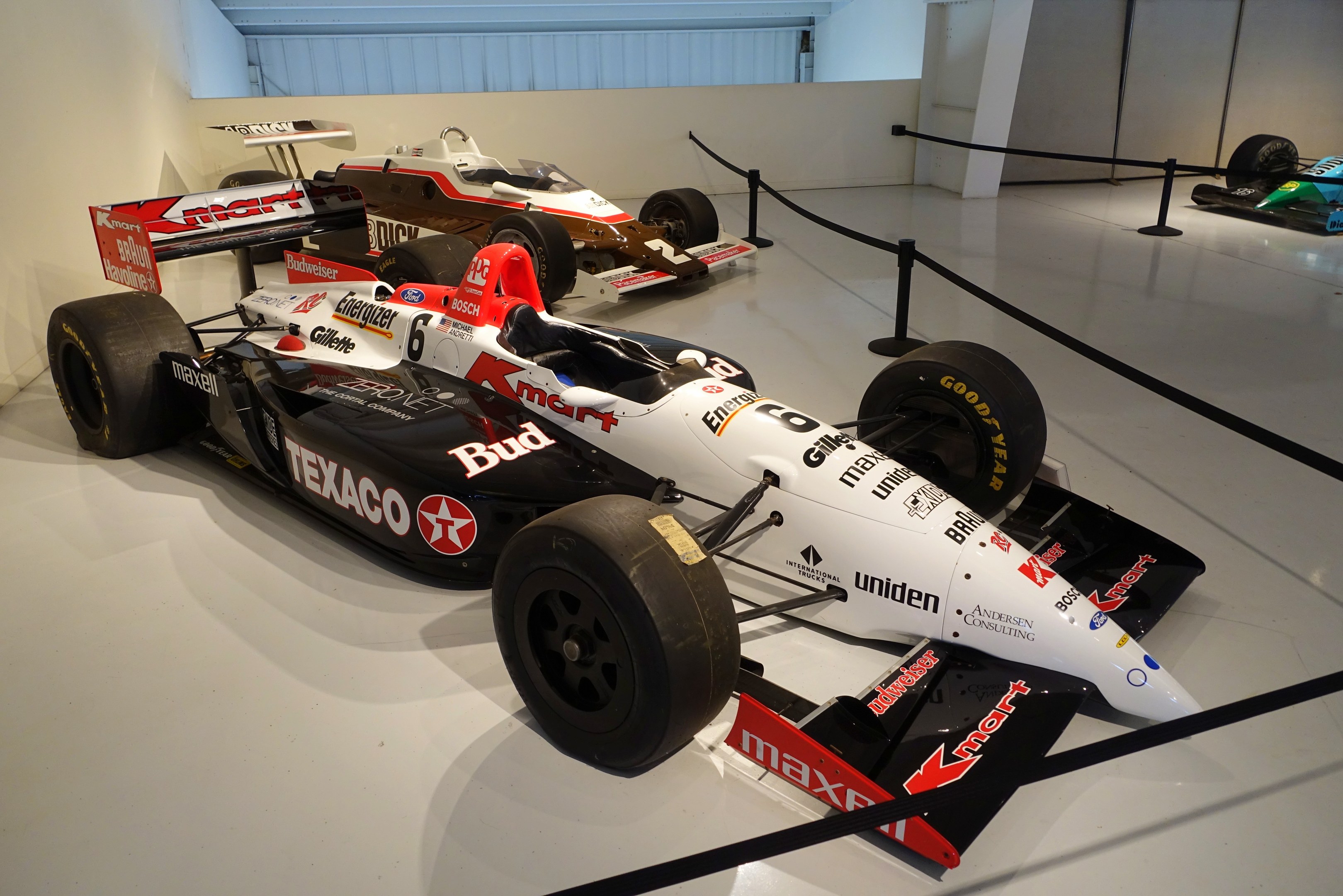 Eine Ausstellung von Rennwagen in einem Museum mit einem Reifen auf dem Boden und einer beleuchteten Decke im Hintergrund.