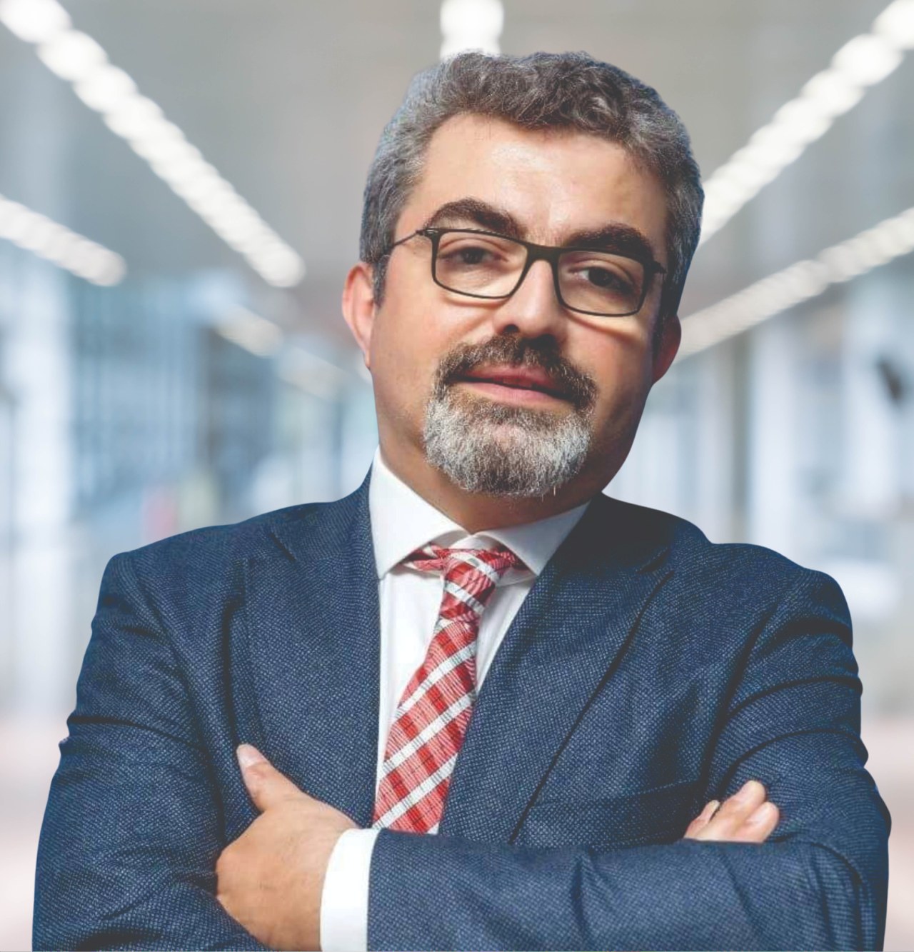 Ein Mann im Anzug und mit Krawatte, der die Arme verschränkt und eine Brille trägt, vor einem unscharfen Hintergrund mit Text, der ihn als neu ernannten Marketingchef identifiziert.