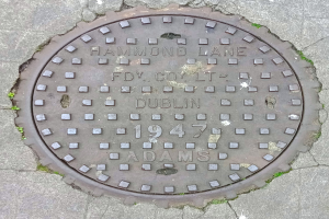 Ein metallener Gullideckel auf einer Straße in Dublin, Irland, mit eingraviertem Text.