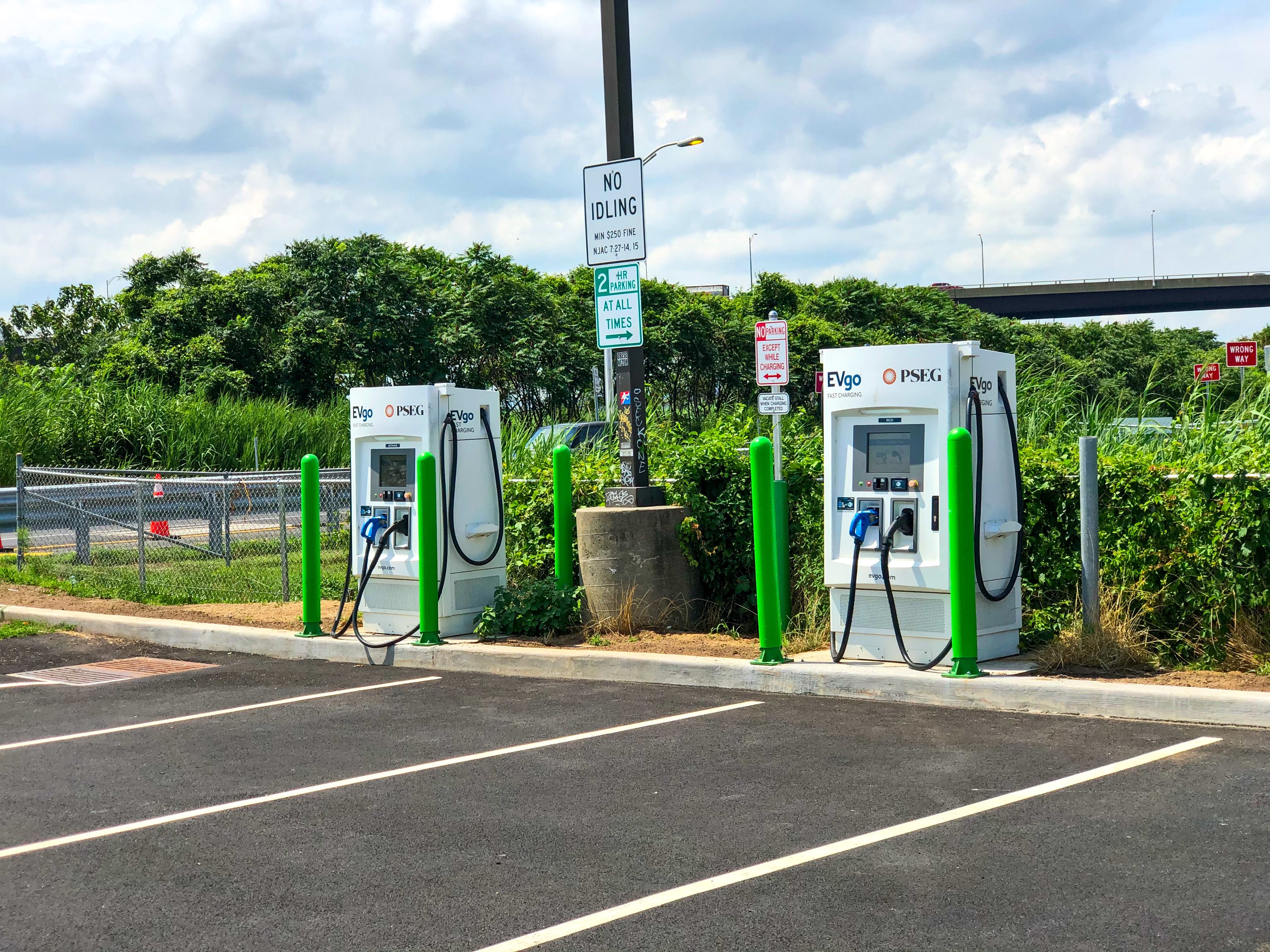 Elektrofahrzeug-Ladestation in einem Parkplatz mit umgebender Infrastruktur, Vegetation und einer bewölkten Himmel.