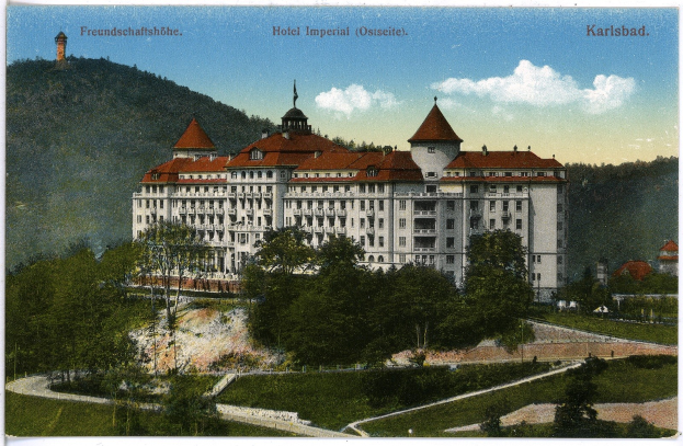 Alte Postkarte des Hotel Imperial in Karlsbad, Deutschland, zeigt ein großes Gebäude mit Fenstern, umgeben von Bäumen, Pflanzen, einem Weg, Hügeln und einem bewölkten Himmel, mit Text oben.