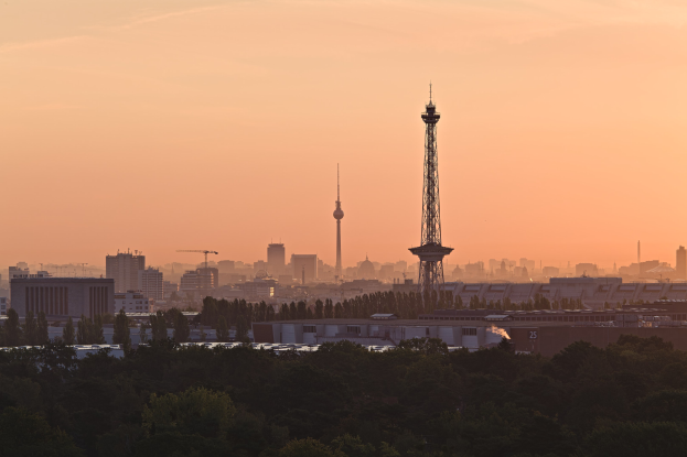 Sunset view of Berlin skyline from a hilltop, featuring buildings, trees, and the TV Tower against a colorful sky.