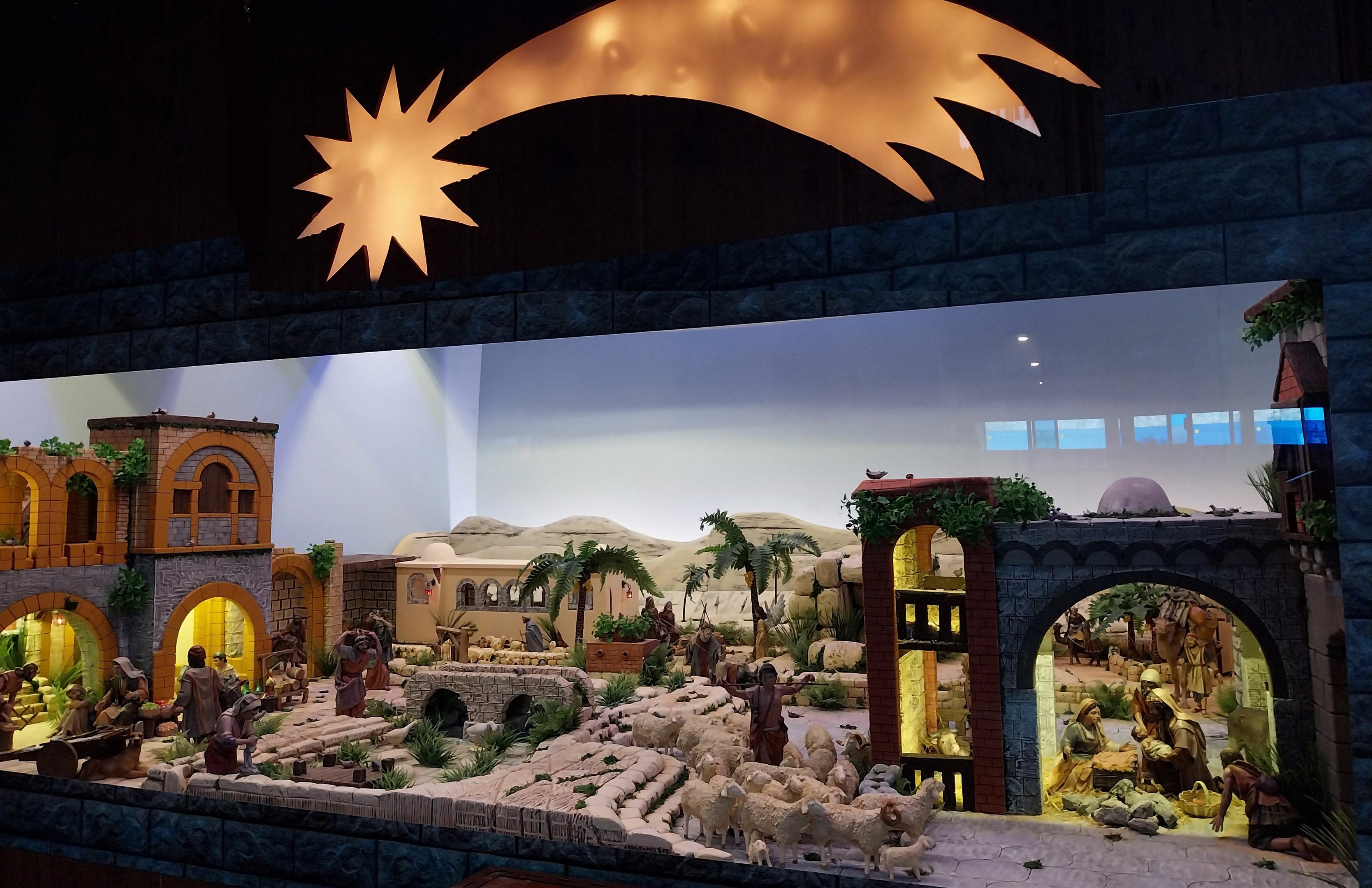 Eine Krippe in einem Museum mit Menschen, Tieren, Häusern, Bäumen und anderen Gegenständen, beleuchtet von oben.