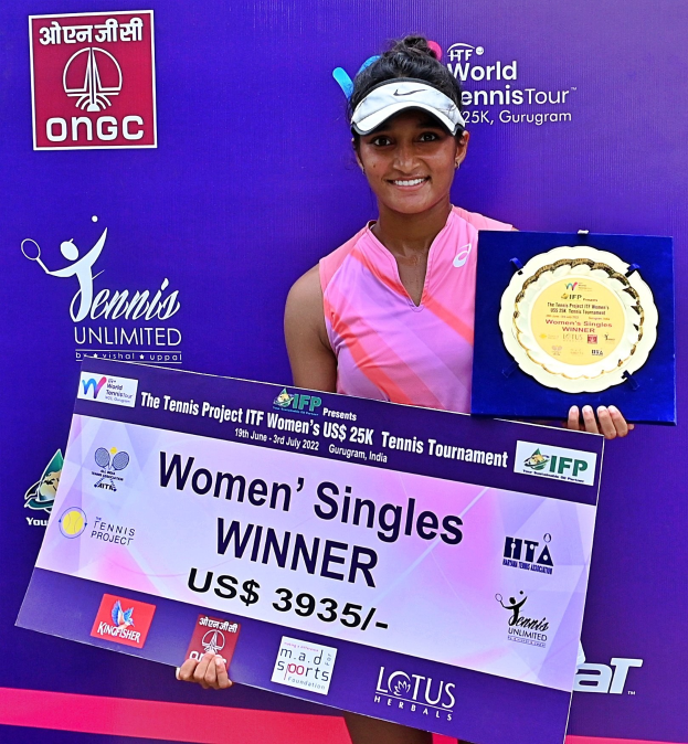 Eine Frau auf einem Tennisplatz hält einen Pokal und eine Tafel mit der Aufschrift "Frauen-Einzel-Siegerin", trägt eine Mütze mit einem Banner im Hintergrund.