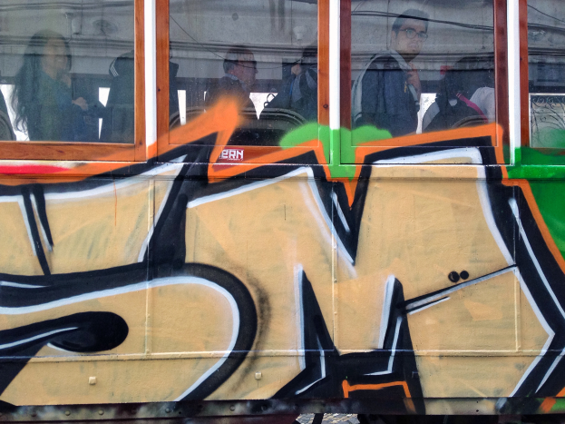 Ein Zug mit Graffiti an der Seite, der Passagiere im Inneren zeigt und ein Gebäude und den Himmel durch seine Fenster reflektiert.