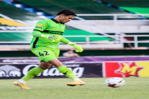 Ein Torwart in grüner Uniform kickt einen Fußball auf einem Rasenfeld in einem Stadion, mit Bannern im Hintergrund, die "Chivas USA vs Mexico City, 3-1, Copa Libertadores" lesen.