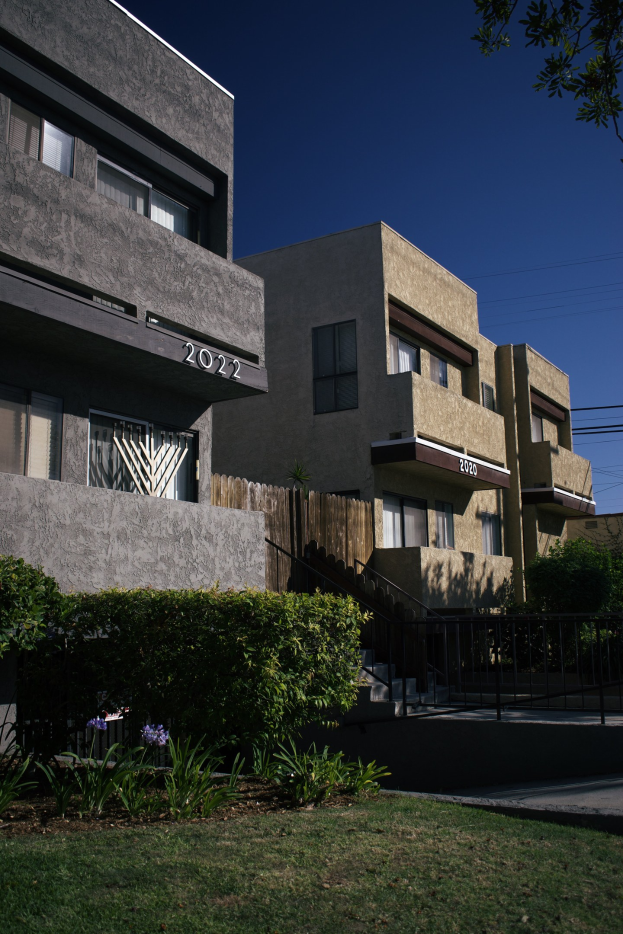 Eine Reihe von Wohngebäuden in San Francisco, Kalifornien, mit sichtbaren Fenstern, Pflanzen, Gras, einem Zaun, Treppen, einem Baum und einem Himmel als Hintergrund.