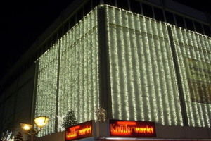 Ein festlich geschmücktes Gebäude in Berlin, Deutschland, mit Weihnachtslichtern umgeben von Bäumen und Laternenmasten, mit Texttafeln in der Nähe und dem Himmel im Hintergrund.