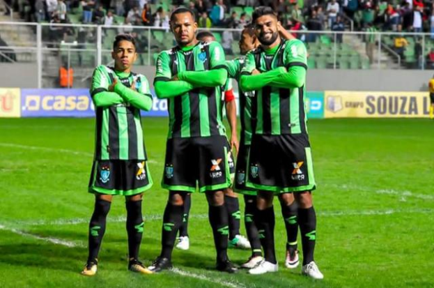 Eine Gruppe von Männern in grünen und schwarzen Kleidern steht auf einem Fussballfeld und feiert, mit einer Menge und Stadionstrukturen im Hintergrund.