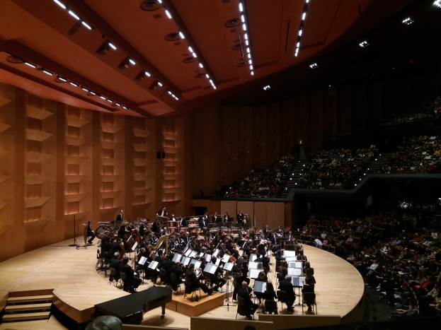 Ein großes Auditorium voller Menschen bei einem Konzert in der Royal Albert Hall in London, mit Künstlern auf der Bühne und Lampen an der Decke.