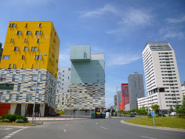 Eine Straße in der Stadt mit hohen Gebäuden, die als Teil der Universität Rotterdam gekennzeichnet sind, Straßenmäste, Straßenlaternen, Kraftfahrzeuge, Informationsschilder, Büsche, Bäume und ein bewölkter Himmel.