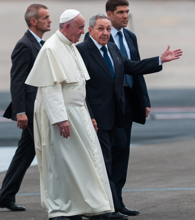Papst Franziskus in einem weißen Gewand und Hut, begleitet von vier Männern in schwarzen Anzügen und Krawatten, beim Ankommen am Flughafen im Petersplatz im Vatikan.