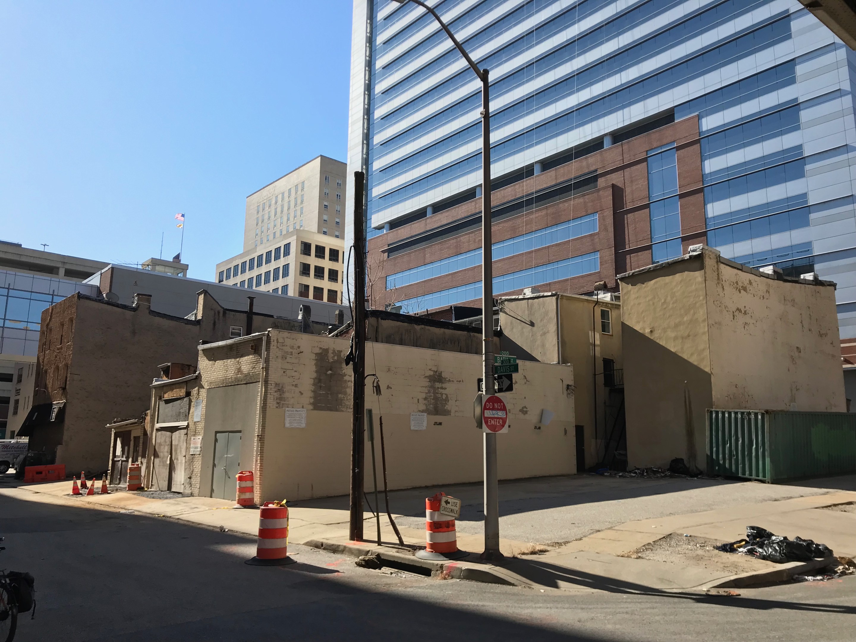 Eine Stadtstraße mit einem geparkten Fahrrad, umgeben von Gebäuden, Straßenmöbeln, Kraftfahrzeugen und einer abgerissenen Gebäude im Hintergrund unter einem klaren blauen Himmel.