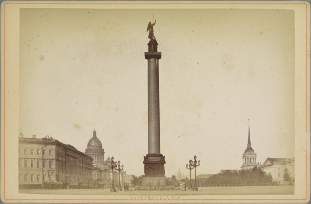 Ein altes Foto eines Denkmals in einer Stadt, umgeben von Gebäuden, Straßenlaternen, Bäumen und einem klaren Himmel, mit Text am unteren Bildrand.