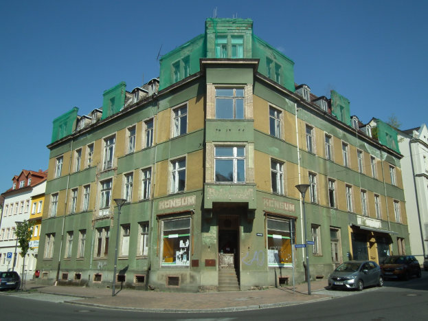 Altes Grünfassade-Gebäude an einer Straßenecke mit Fahrzeugen, Straßenmäständen, Lichtern, Bäumen und einem klaren Himmel.