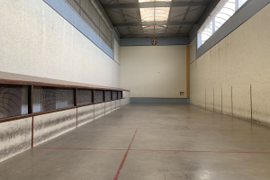 Ein leerer Turnraum mit einer roten Linie auf dem Boden, Wänden, einer Decke mit Lampen und einigen Gegenständen, der sich in einem Gebäude mit einem Tennisplatz in der Mitte befindet.