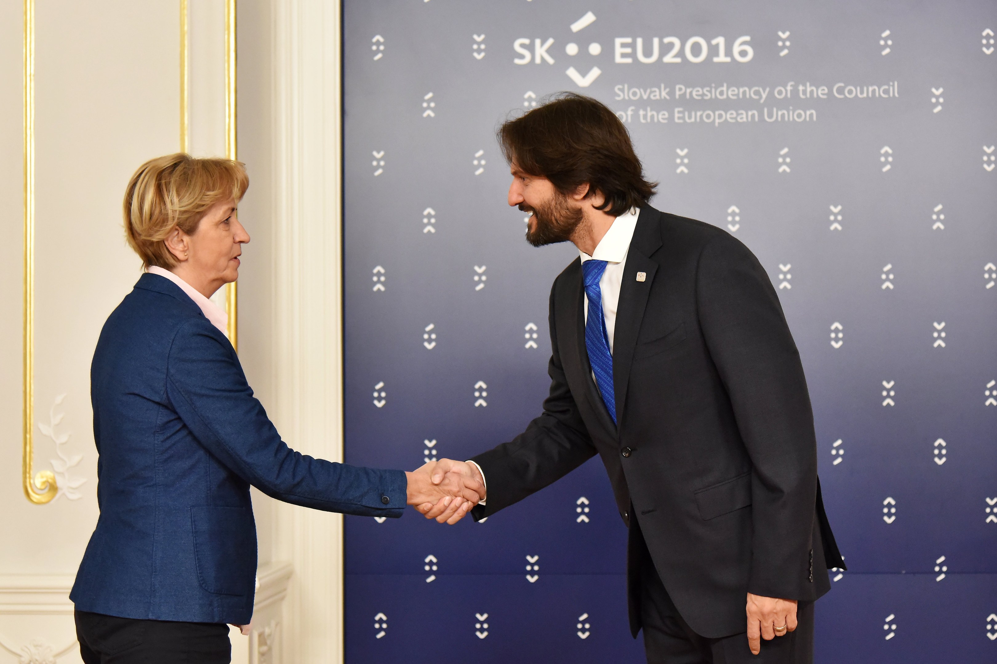 Bundeskanzlerin Angela Merkel und Bundespräsident Joachim Gauck schütteln sich vor einer Wand mit einem 'EU-Gipfel'-Schild und einer Tür im Hintergrund die Hände, beide lächeln.