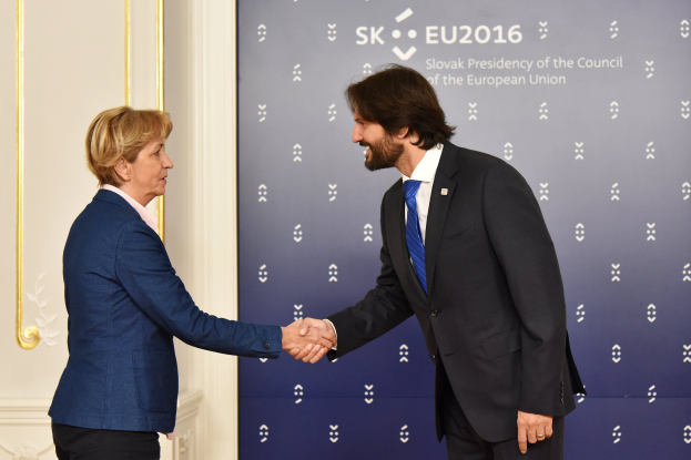 Bundeskanzlerin Angela Merkel und Bundespräsident Joachim Gauck schütteln sich vor einer Wand mit einem 'EU-Gipfel'-Schild und einer Tür im Hintergrund die Hände, beide lächeln.