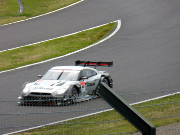 Audi R8 LMS GT3 auf der Nürburgring 24 Stunden Rennstrecke positioniert, umgeben von einem Metallzaun und grünem Gras, mit der Strecke, die sich vor ihm erstreckt.